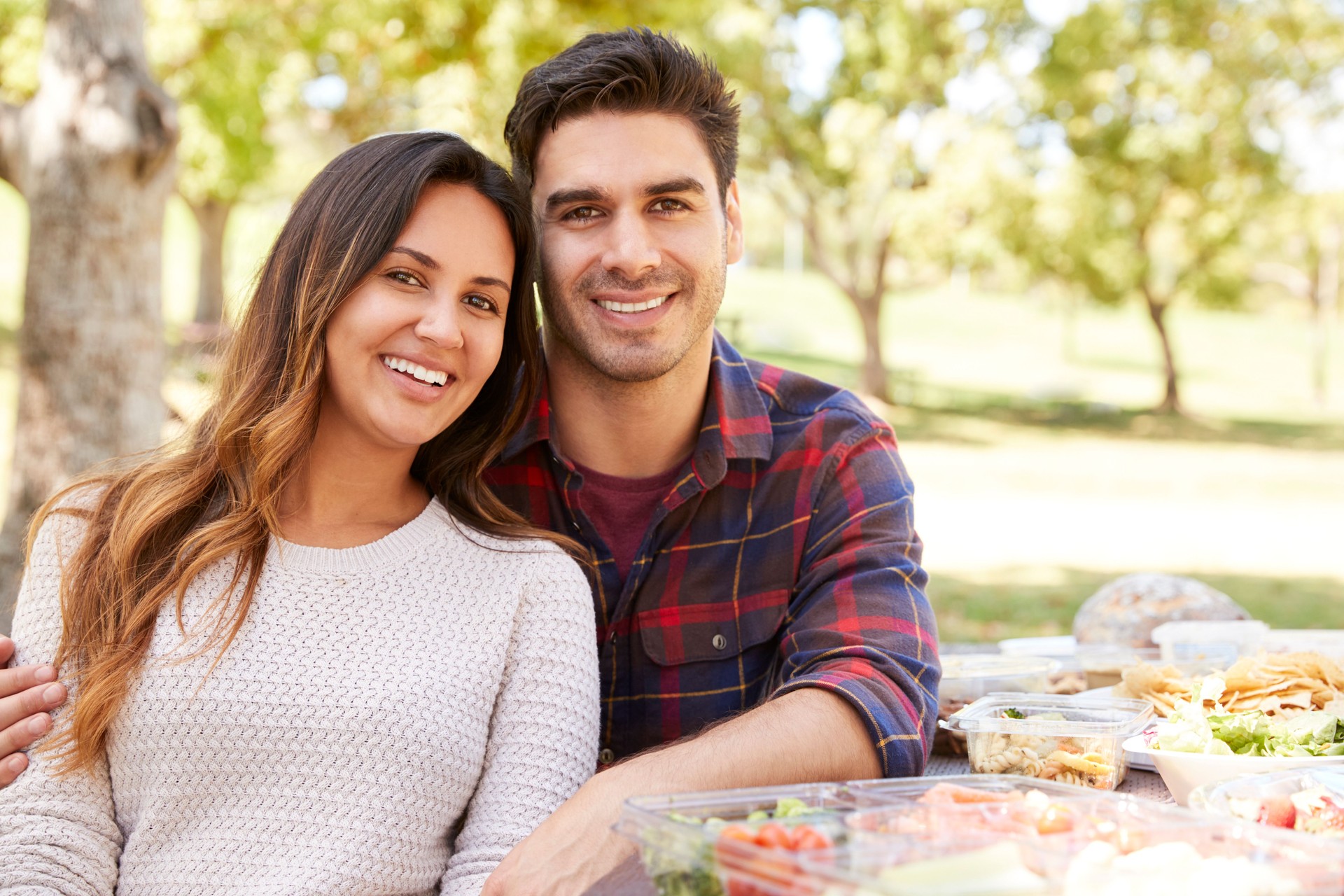 Young couple sitting at picnic table smiling to camera