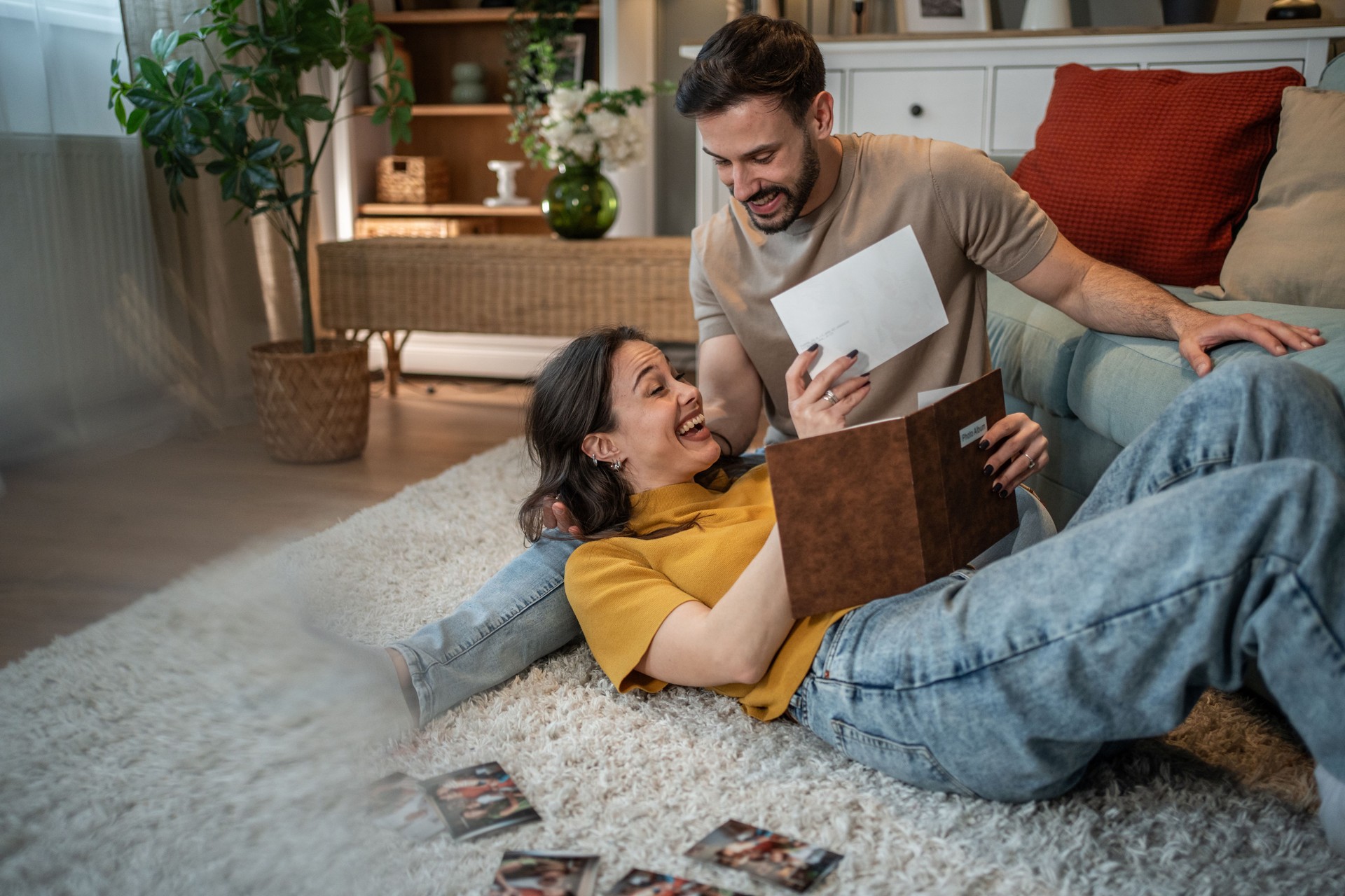 Happy couple lying on carpet and watching old photos in album at home